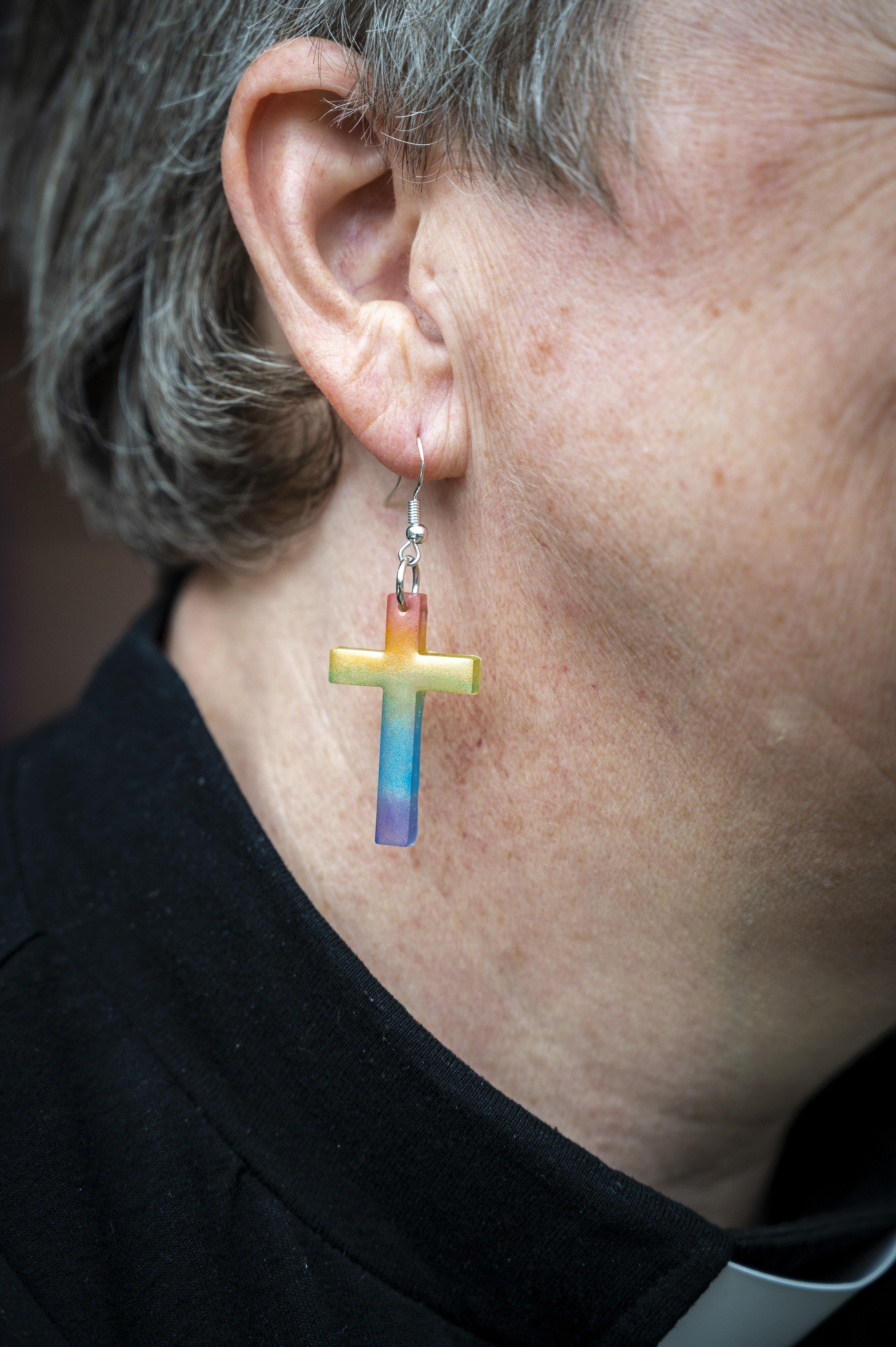 I ett öra hänger ett regnbågsfärgat kors.