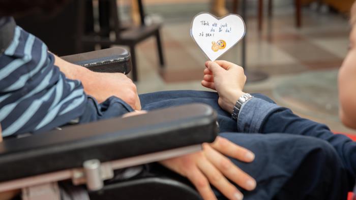 Ett barn i rullstol får ett hjärta med texten Tänk att just du är du – så bra!