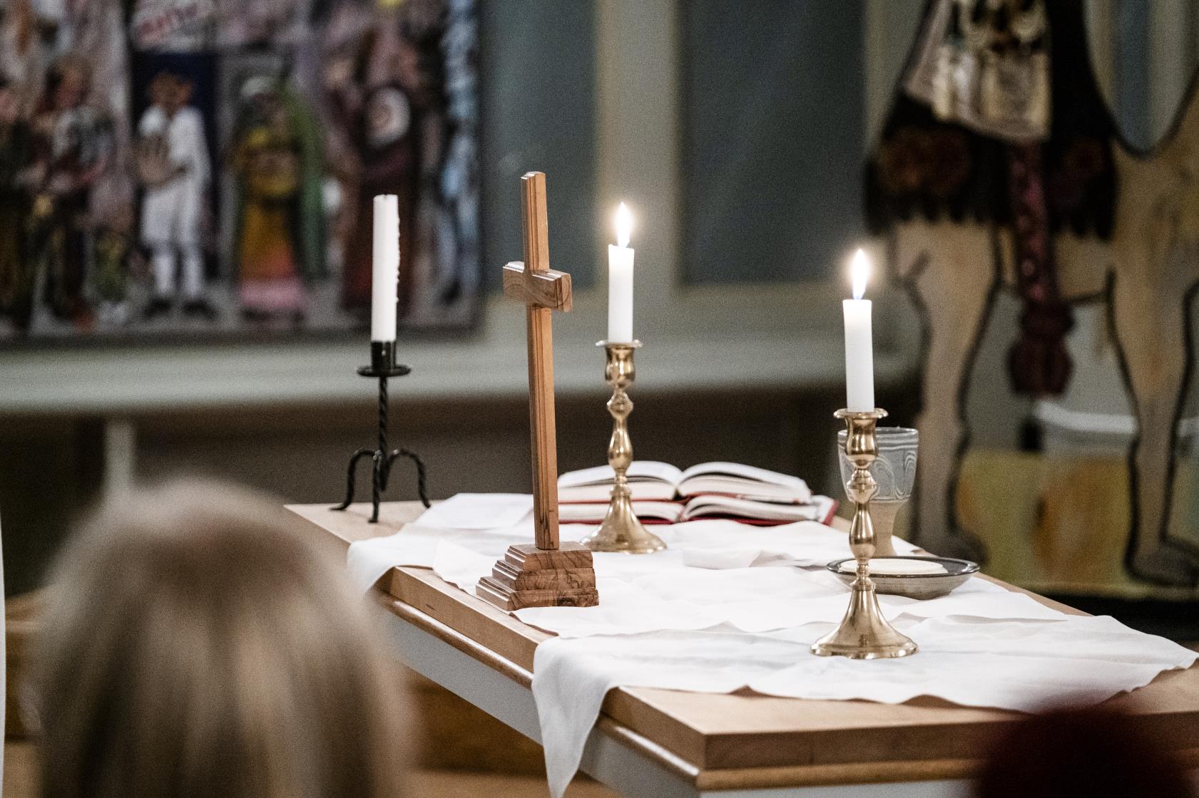 Ett litet träkors och tre ljusstakar med tända ljus står på ett altare.