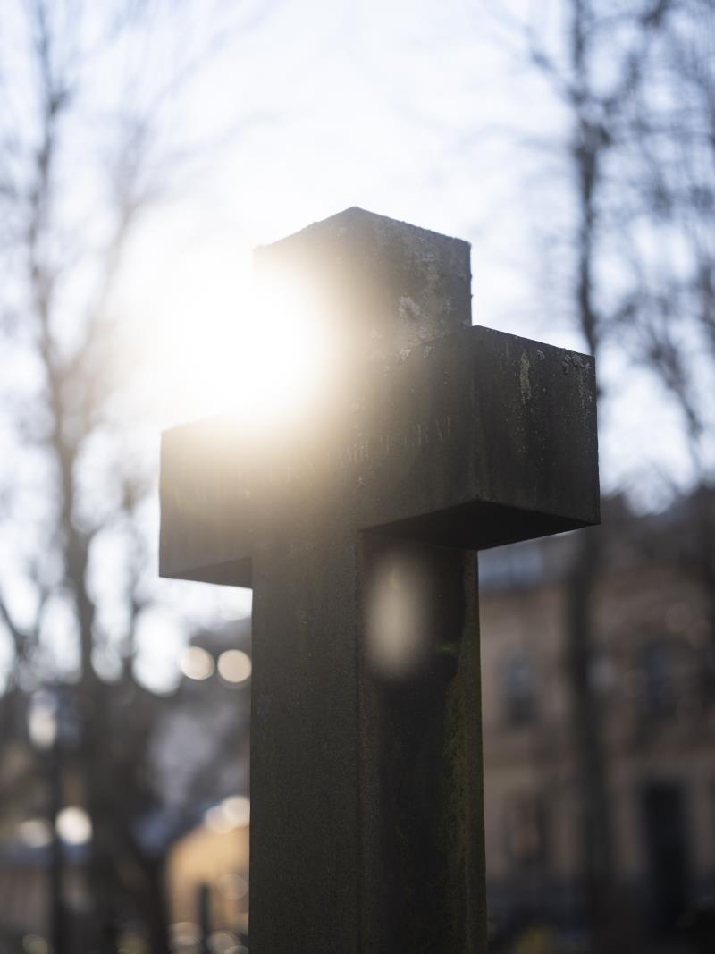 Ett kors på en gravsten i motljus.