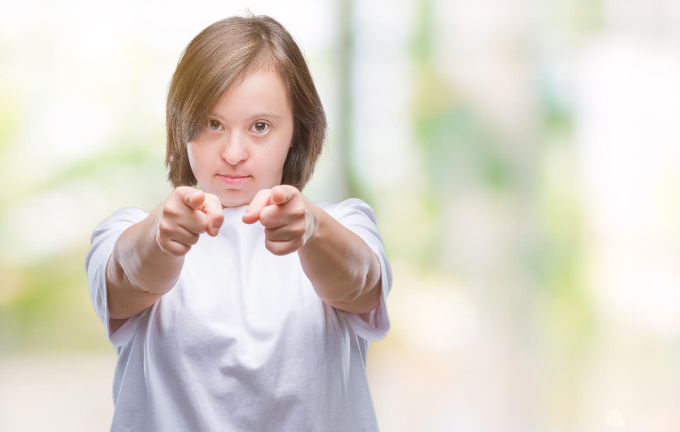Young adult woman with Down syndrome over isolated background pointing fingers to camera with happy and funny face. Good energy and vibes.
