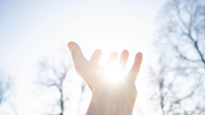 Någon håller upp en hand mot solen och det ser ut som att solen ligger i handflatan.