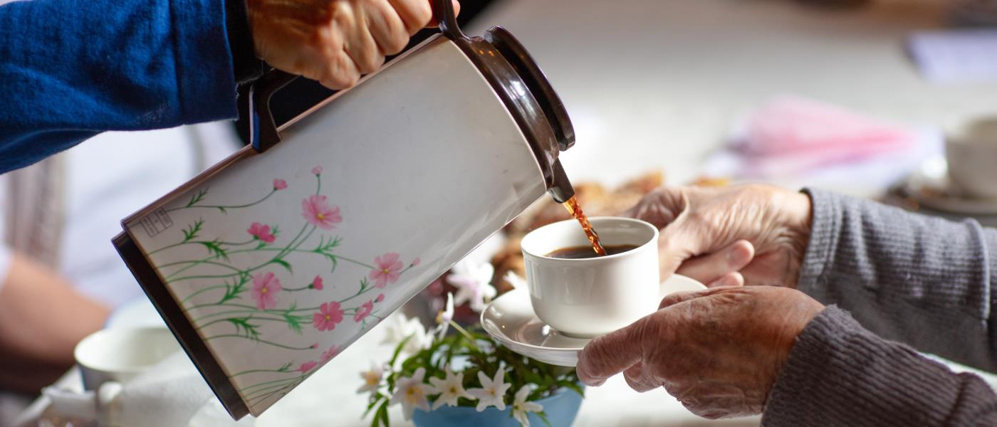 Någon häller upp kaffe från en blommig termos till någon som håller fram sin kopp.