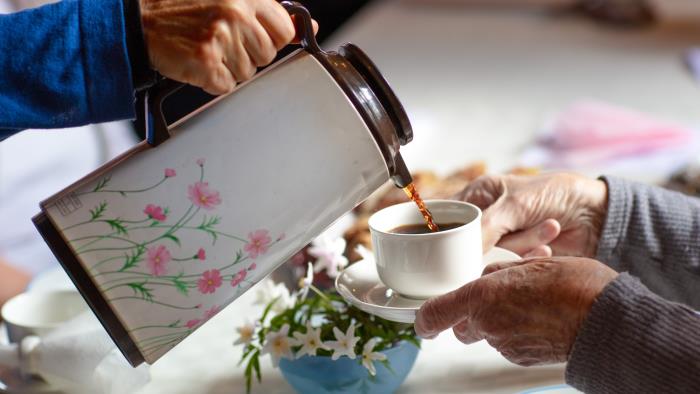 Någon häller upp kaffe från en blommig termos till någon som håller fram sin kopp.