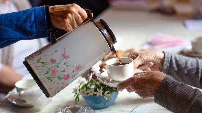 Någon häller upp kaffe från en blommig termos till någon som håller fram sin kopp.