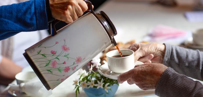 Någon häller upp kaffe från en blommig termos till någon som håller fram sin kopp.