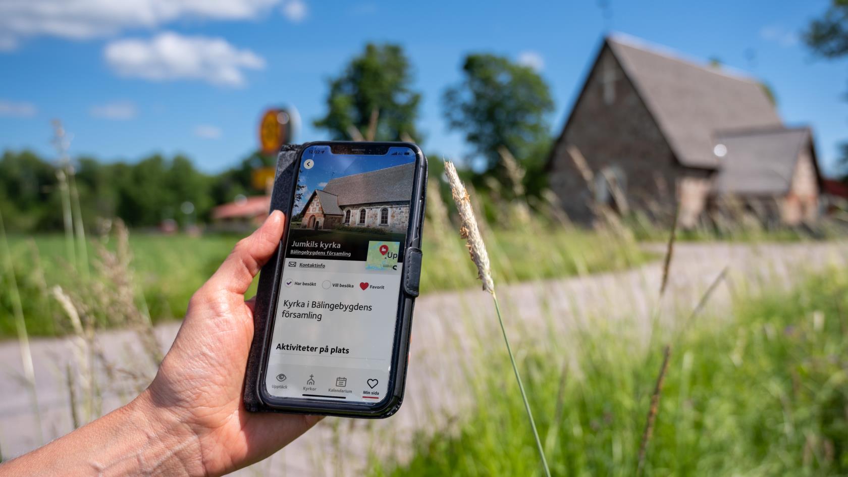 En person som kommit fram till en gammal kyrka håller en mobiltelefon i handen. På skärmen visas kyrkans namn och position på en karta.