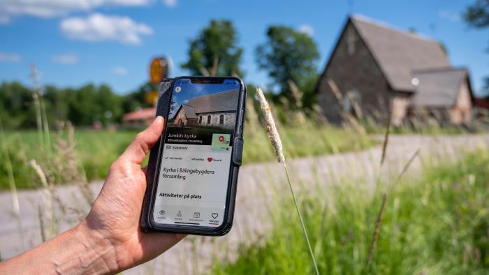 En hand håller i en mobil med skärmbild om kyrkguiden som visar adressen för kyrkan.