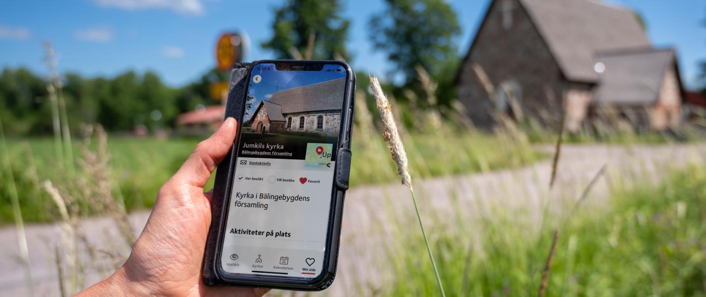En hand håller i en mobil med skärmbild om kyrkguiden som visar adressen för kyrkan.