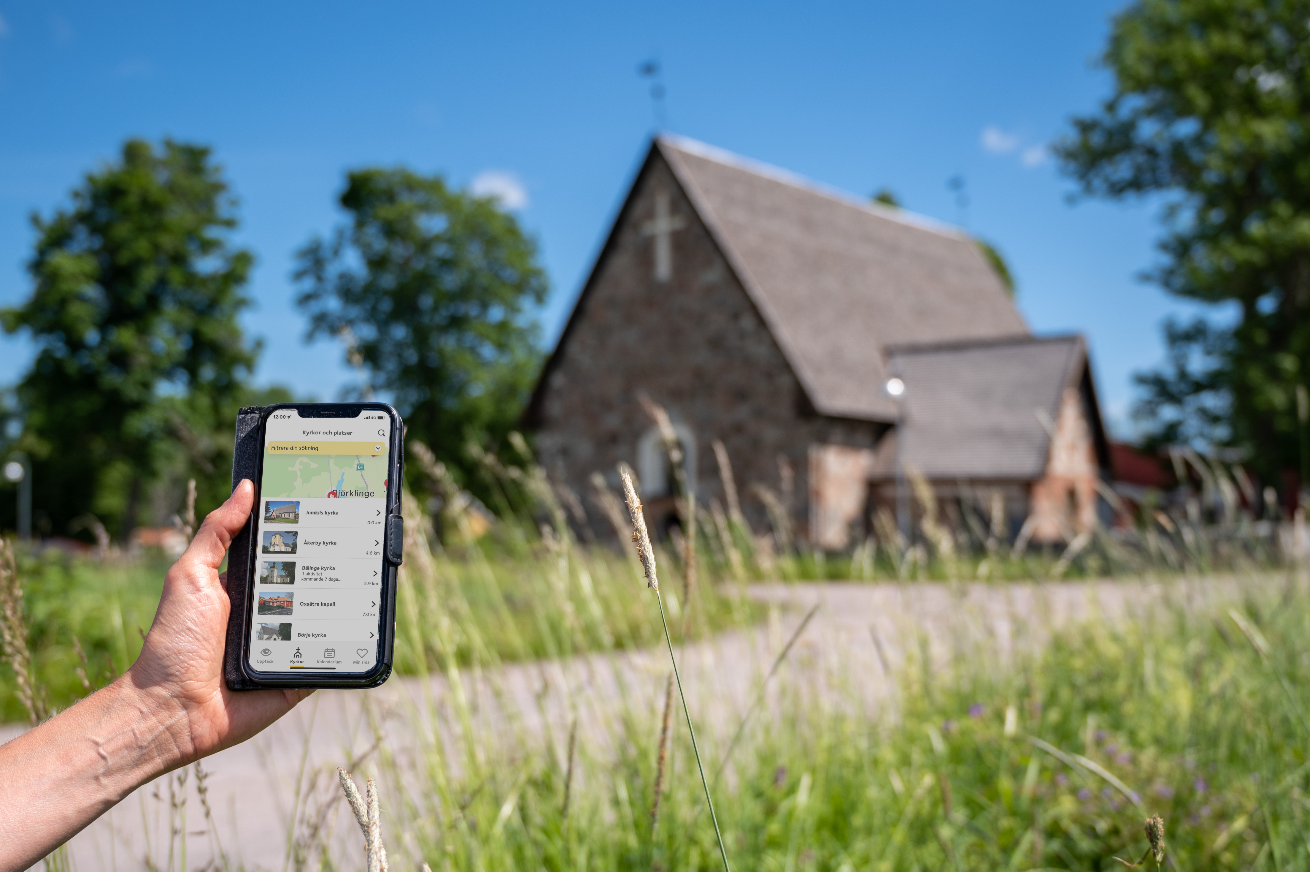 En person som kommit fram till en gammal kyrka håller en mobiltelefon i handen. På skärmen visas information om kyrkan.