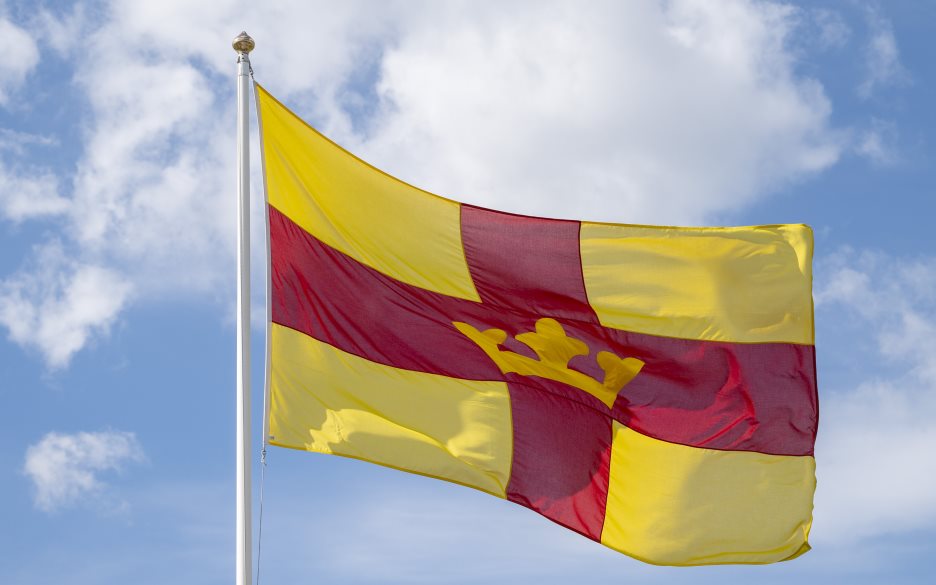 En flaggstång med Svenska kyrkans flagga mot en blå himmel.