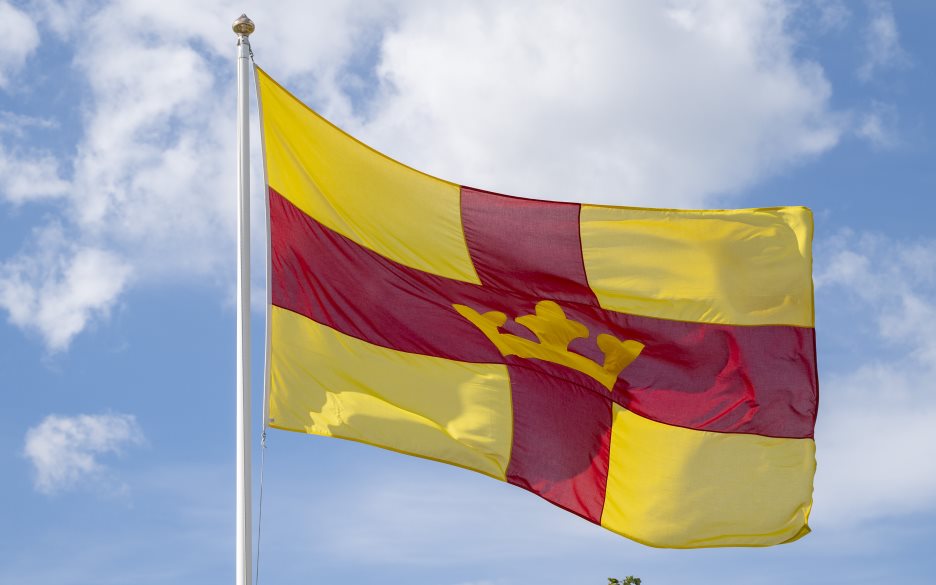 En flaggstång med Svenska kyrkans flagga mot en blå himmel.