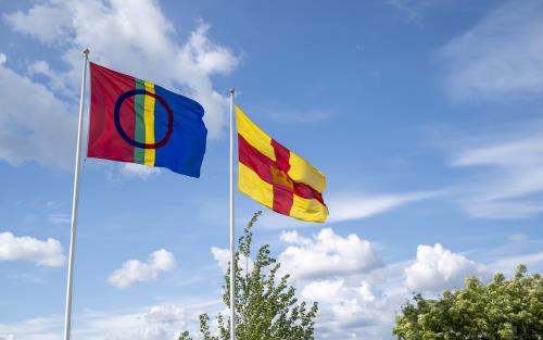 Två flaggstänger med den samiska flaggan och Svenska kyrkans flagga mot en blå himmel.