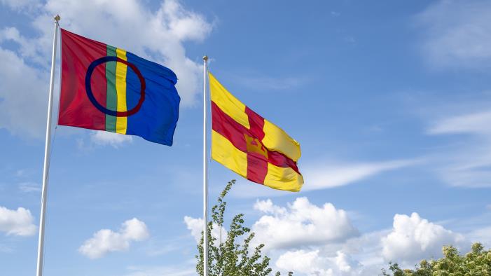 Två flaggstänger med den samiska flaggan och Svenska kyrkans flagga mot en blå himmel.