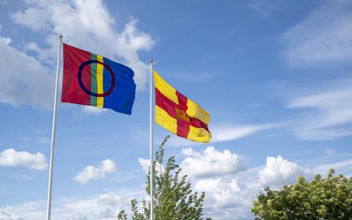 Två flaggstänger med den samiska flaggan och Svenska kyrkans flagga mot en blå himmel.