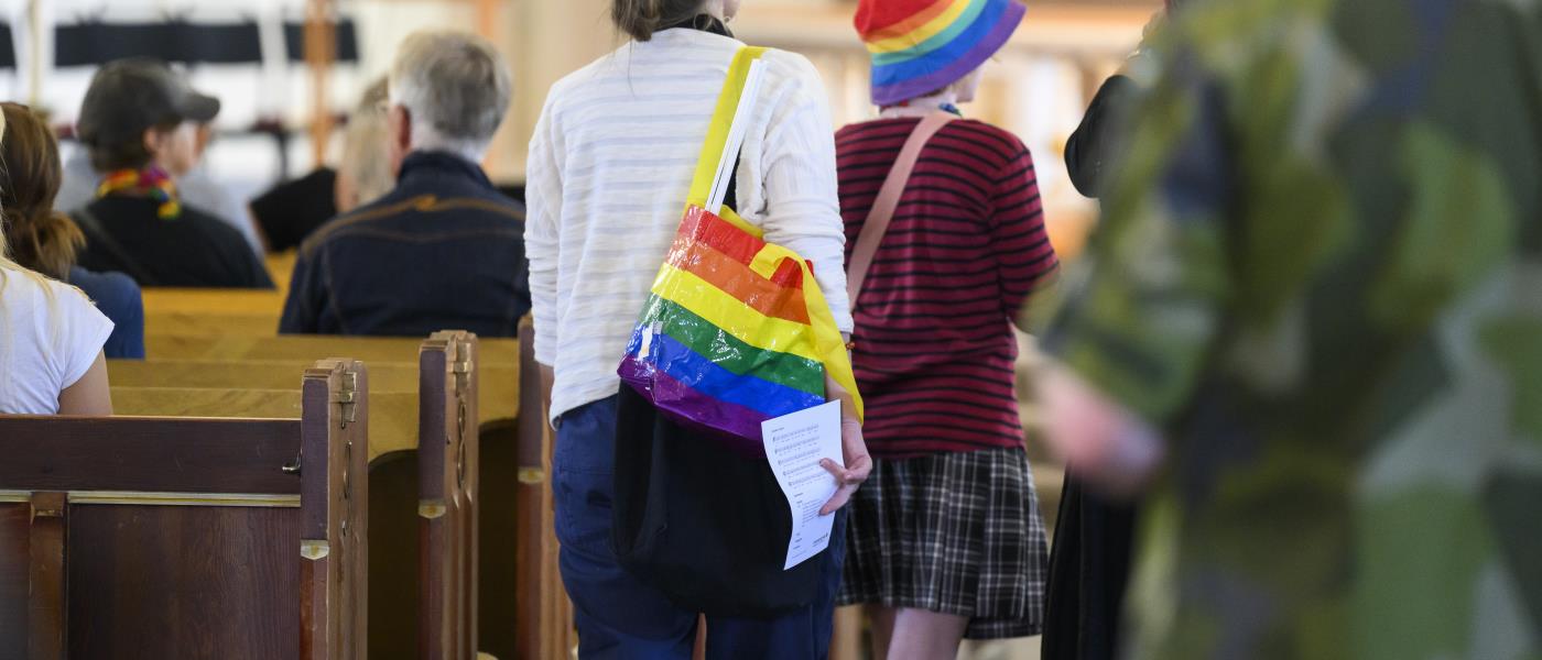 Några personer med regnbågsfärgade accessoarer går i mittgången i en kyrka.