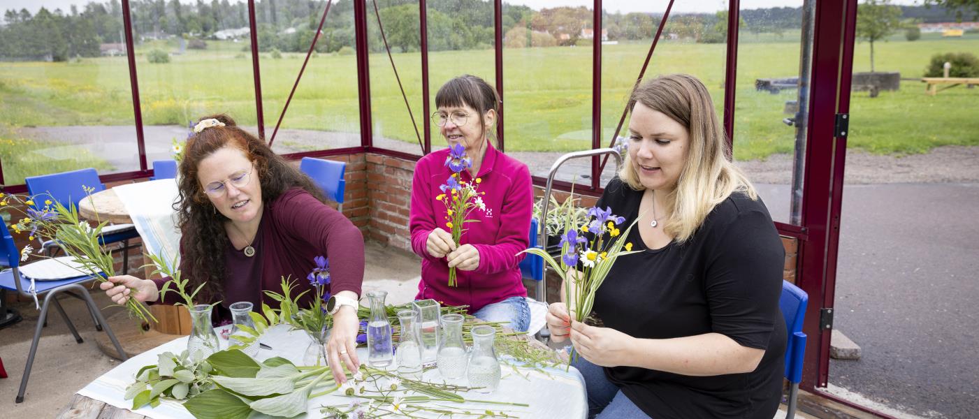 Tre kvinnor sitter på en uteplats och gör buketter av handplockade blommor.
