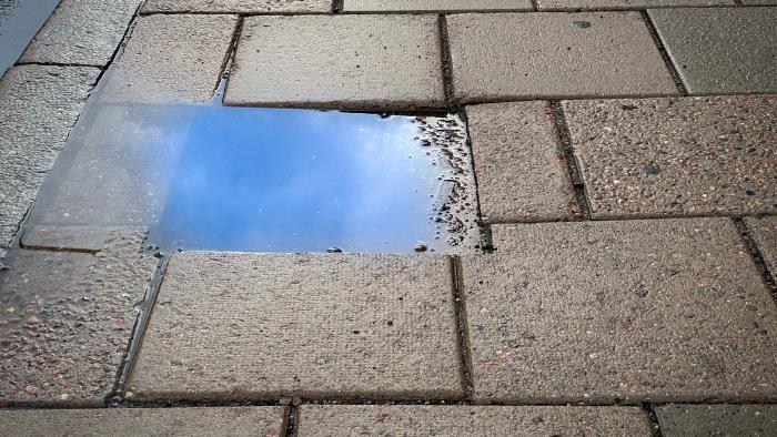 Himlen återspeglas i en vattenpöl på trottoaren.