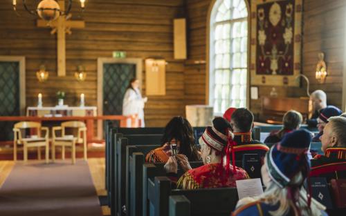Kyrkobesökare i samiska folkdräkter sitter i kyrkbänkarna.