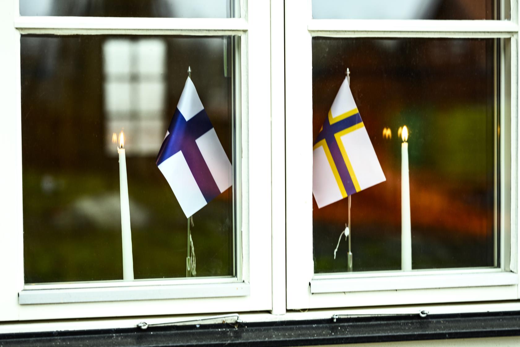 En sverigefinsk och en finsk bordsflagga samt två brinnande stearinljus står i ett fönster.
