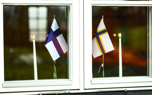 En sverigefinsk och en finsk bordsflagga samt två brinnande stearinljus står i ett fönster.