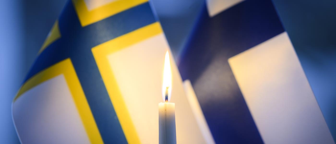 Ett stearinljus brinner framför en finsk och en sverigefinsk bordsflagga.