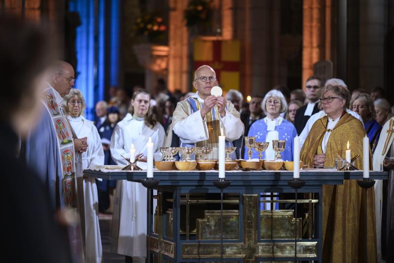 Ärkebiskop Martin Modéus håller upp en oblat ovanför altaret. Personer i högtidsdräkter står runt om.