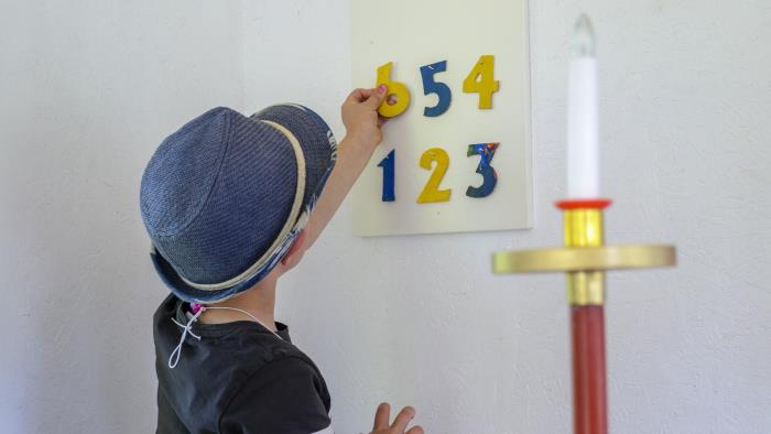 En pojke hänger upp färgglada siffror på en tavla på en psalmtavla. Ett släckt elektriskt ljus i förgrunden.