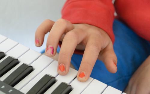 Närbild på en barnhand med avskavt nagellack. Barnet spelar keyboard.