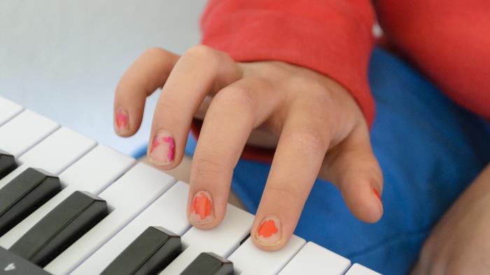 Närbild på en barnhand med avskavt nagellack. Barnet spelar keyboard.