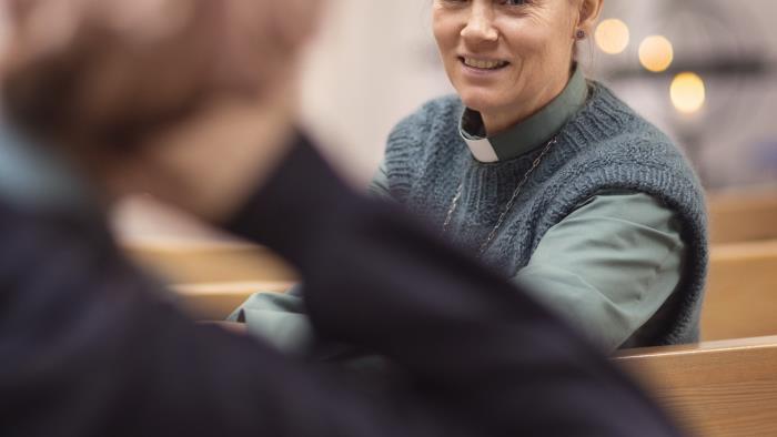 En kvinnlig diakon sitter med någon i kyrkbänken och samtalar.