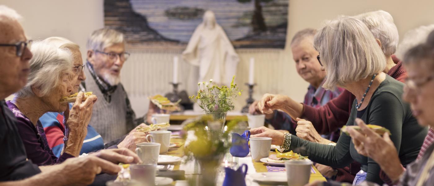 En grupp äldre personer sitter vid ett bord och fikar tillsammans.