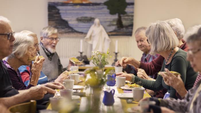 En grupp äldre personer sitter vid ett bord och fikar tillsammans.