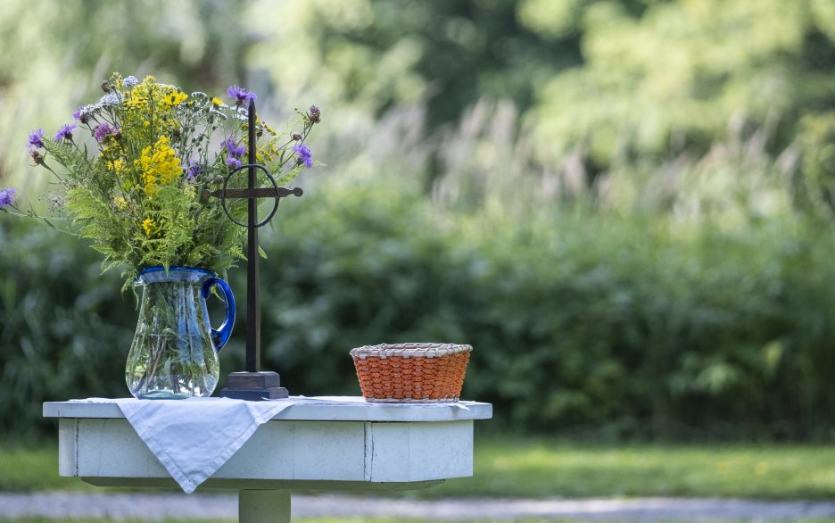 Ett litet träbord har gjort till ett utomhusaltare utsmyckat med ett kors, en liten korg och en blombukett i en vas.
