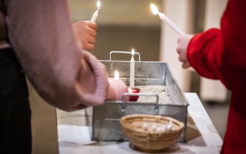Några personer placerar tända stearinljus i en liten plåtlåda fylld med sand.