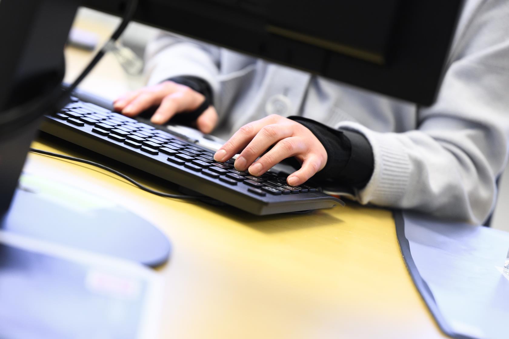 Någon sitter vid ett skrivbord bakom en datorskärm och knappar på ett tangentbord.