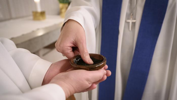 En präst trycker ner sin tumme i en liten skål med aska.