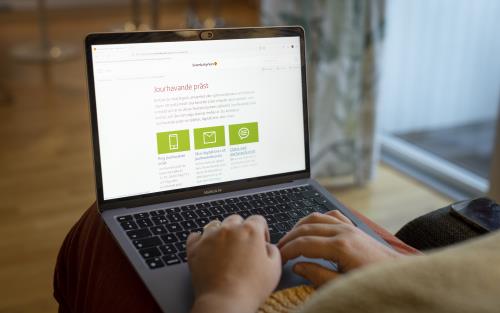 En person sitter vid med en bärbar dator i knät och läser på Svenska kyrkans webbsida om jourhavade präster.