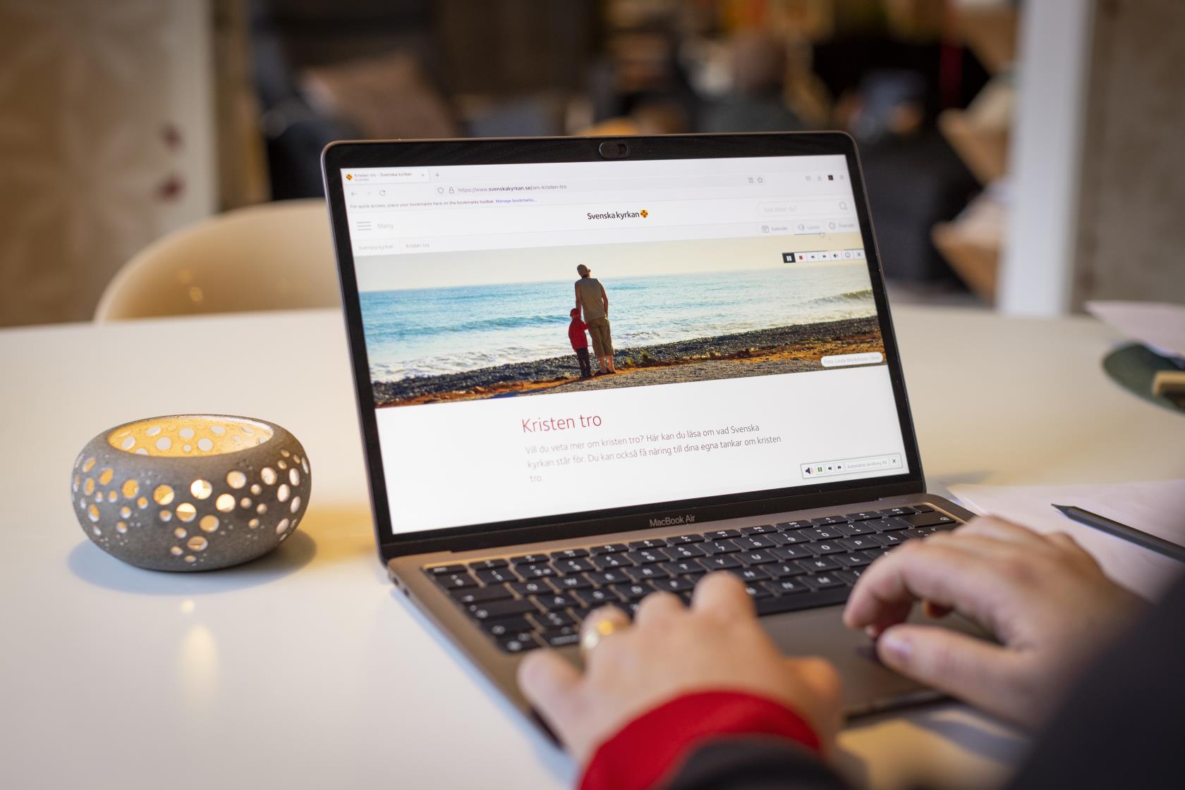 En person sitter vid datorn och läser på Svenska kyrkans webbsida om Kristen tro.