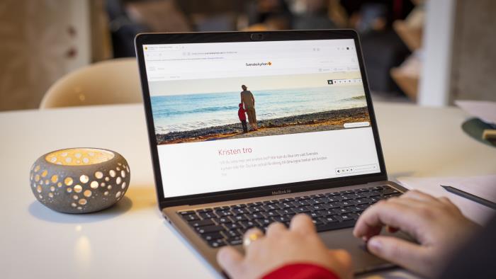 En person sitter vid datorn och läser på Svenska kyrkans webbsida om Kristen tro.