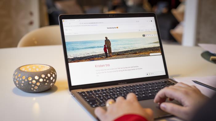 En person sitter vid datorn och läser på Svenska kyrkans webbsida om Kristen tro.