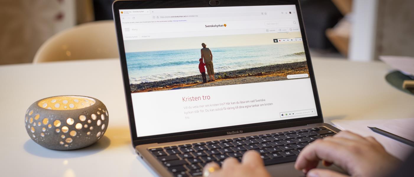 En person sitter vid datorn och läser på Svenska kyrkans webbsida om Kristen tro.