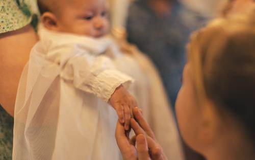 En bebis i dopklänning. Någon håller i barnets hand.