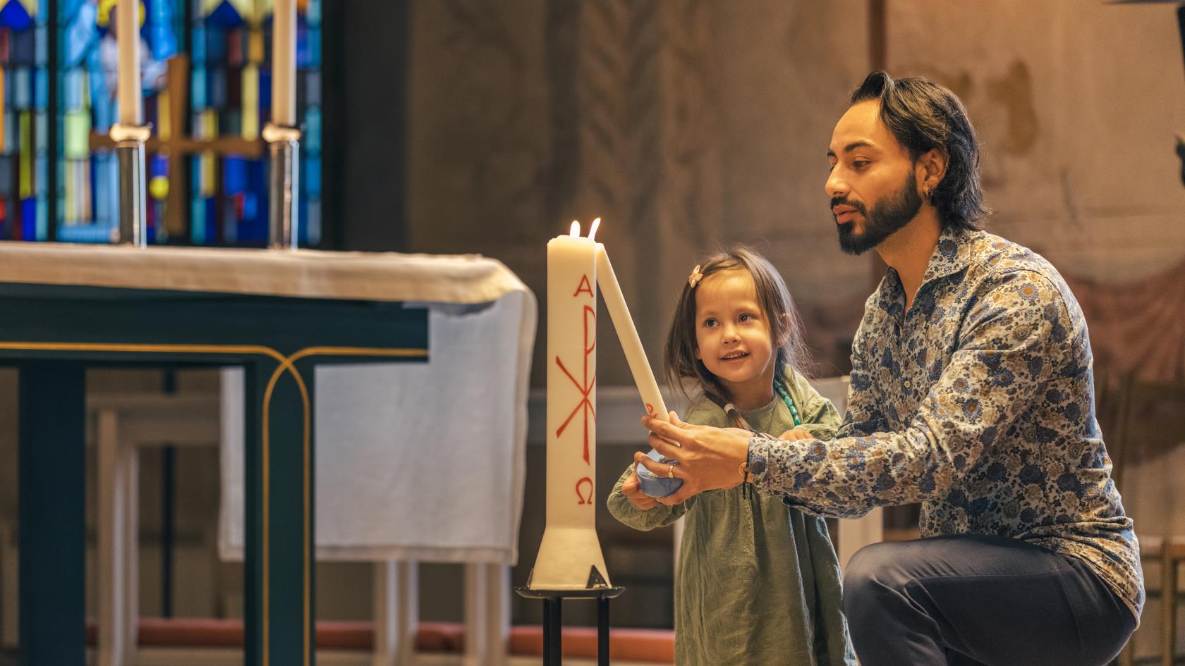 En man och en liten flicka tänder ett dopljus i kyrkan.