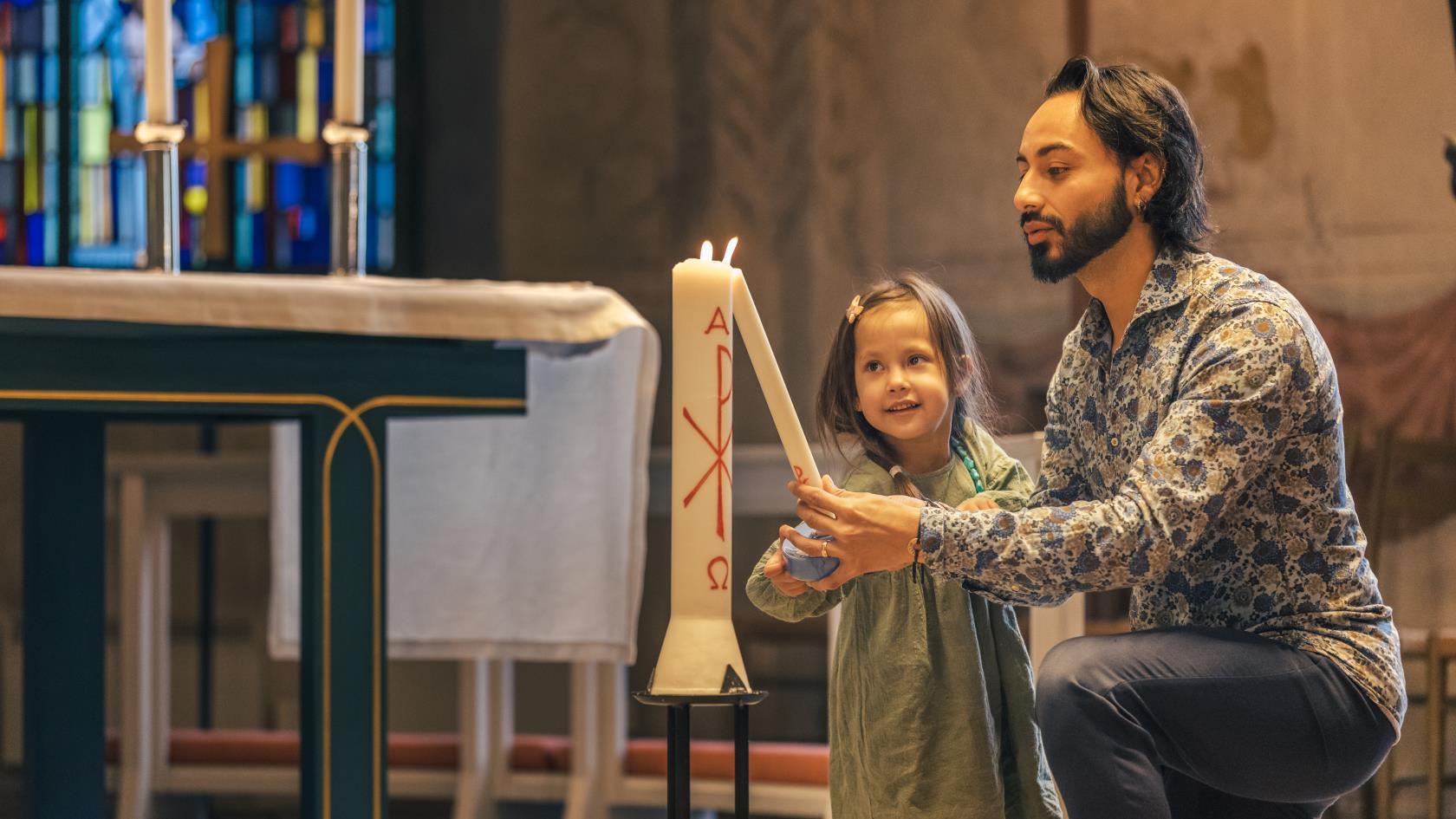 En man och en liten flicka tänder ett dopljus i kyrkan.