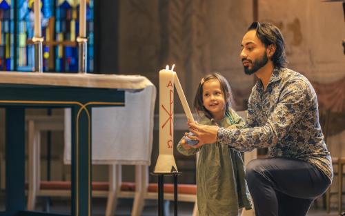 En man och en liten flicka tänder ett dopljus i kyrkan.