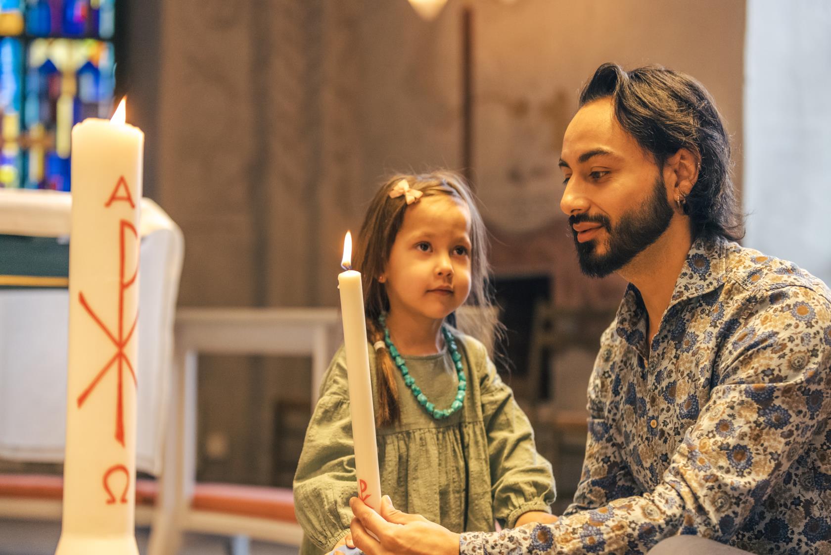 En man och en liten flicka tänder ett dopljus i kyrkan.