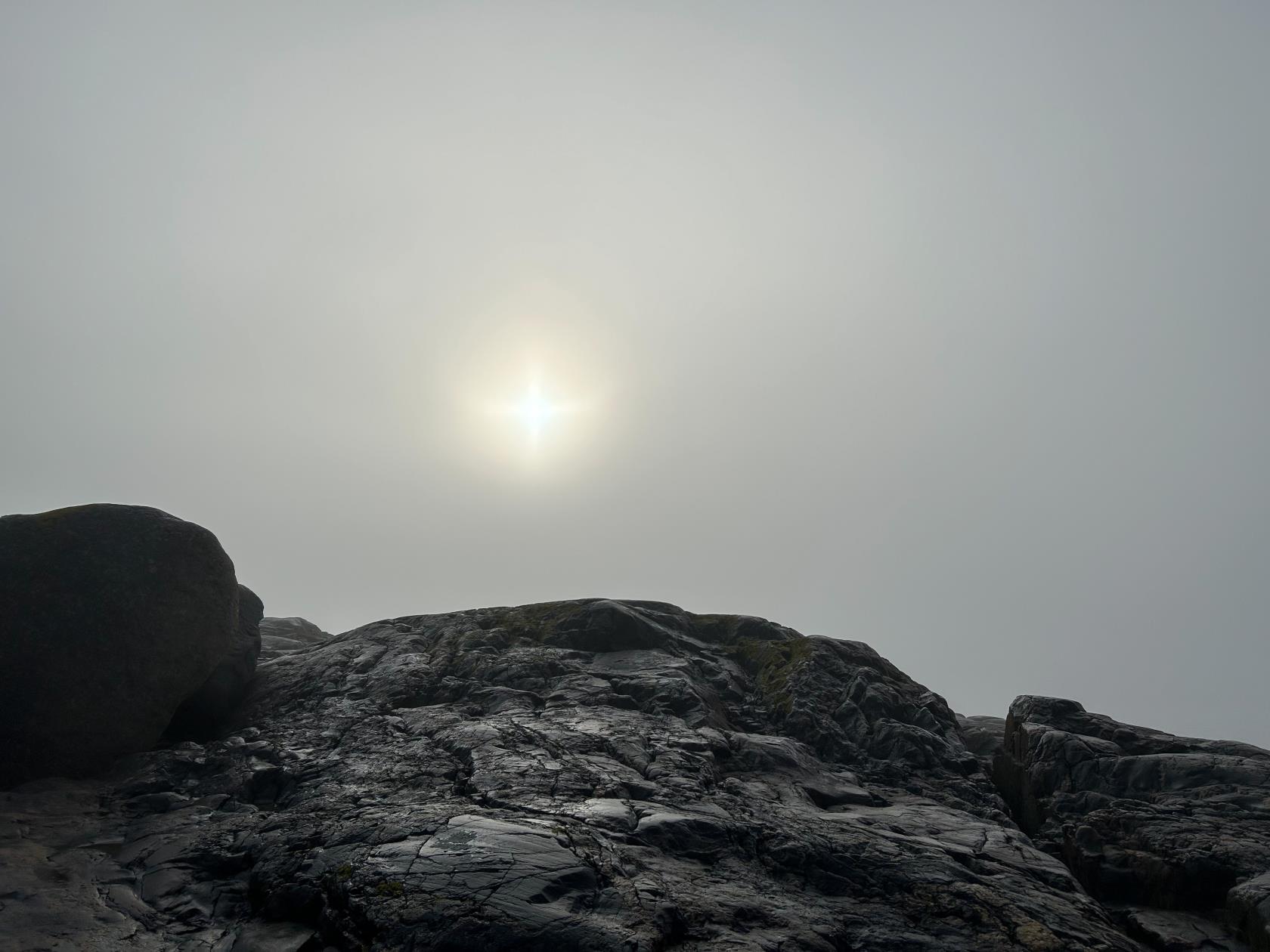 Närbild på klippor. Solen syns svagt genom en disig himmel.