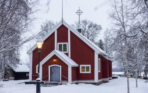 En liten röd träkyrka i ett snöigt landskap.