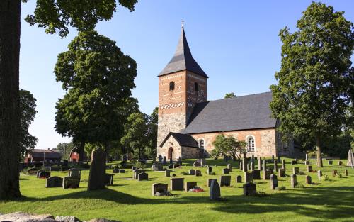 En kyrka i sten och rött tegel. Gravstenar på en grön gräsmatta.